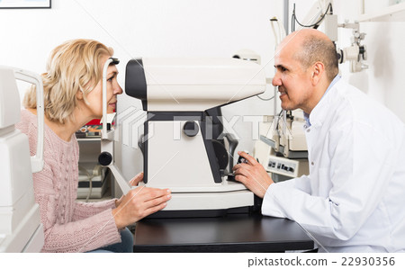 Mature optician examinating eyesight with aid of slit lamp Mature optician examinating eyesight with aid of slit lamp 22930356