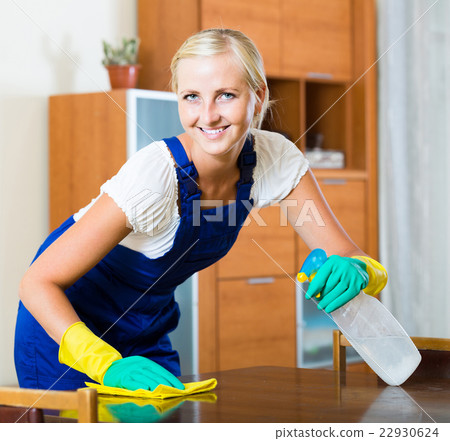 blonde girl in uniform dusting in room and smiling 22930624