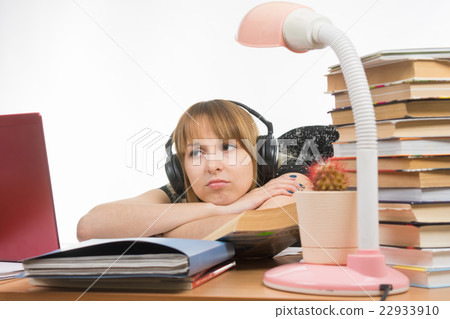 Girl sad student sitting at the table wearing headphones and listening to music Girl sad student sitting at the table wearing headphones and listening to music 22933910