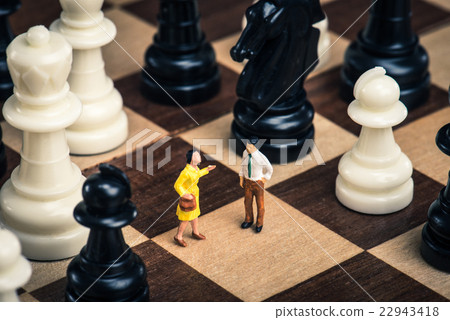A miniature man standing on a chessboard.Gen relationship 22943418