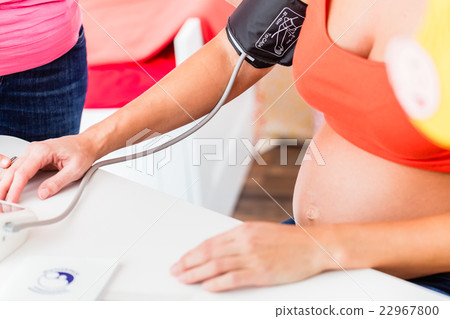Pregnant woman with baby-bump and blood pressure cuff during che 22967800