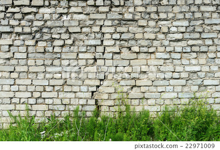 Old white brick wall with crack and green grass 22971009