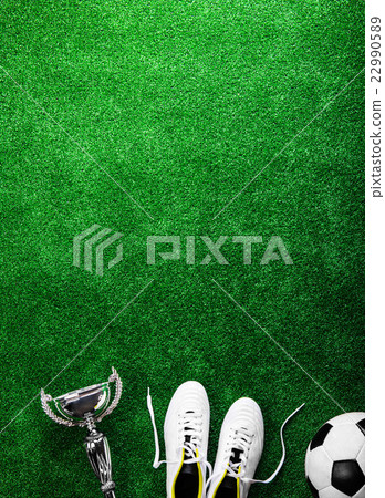 Soccer ball, cleats and trophy against green 22990589