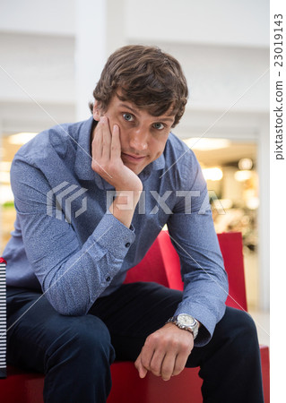 Man sitting in shopping mall with bored expression Man sitting in shopping mall with bored expression 23019143