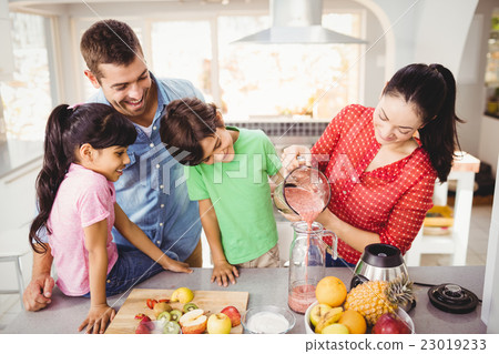 Smiling family with mother pouring fruit juice Smiling family with mother pouring fruit juice 23019233