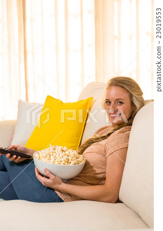 Pretty blonde watching TV and eating pop corn 23019553