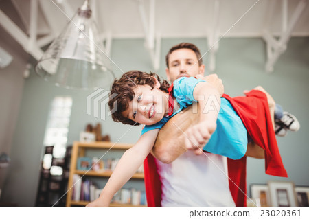 Portrait of father carrying son wearing superhero costume 23020361