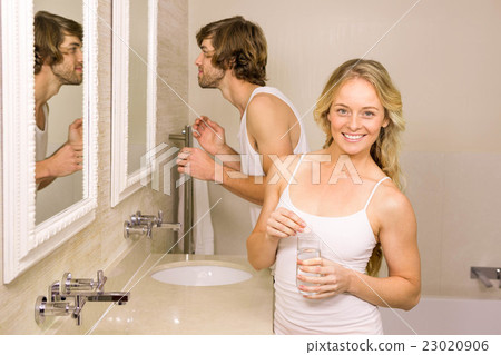 Blonde woman taking a pill with her boyfriend brushing his teeth Blonde woman taking a pill with her boyfriend brushing his teeth 23020906