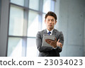 A businessman with a 30's standing with a tablet at the window of the office building 23034023