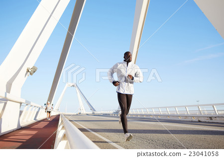 Dark skinned runner jogging against bright sky Dark skinned runner jogging against bright sky 23041058