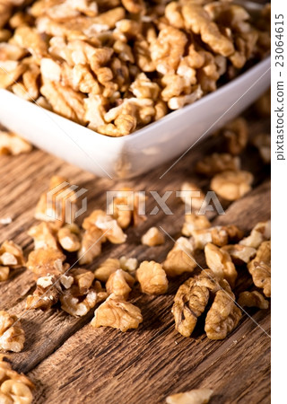Several walnuts spilled around white bowl on wood Several walnuts spilled around white bowl on wood 23064615
