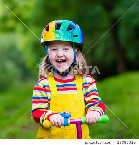 Little girl riding a colorful scooter Little girl riding a colorful scooter 23080026
