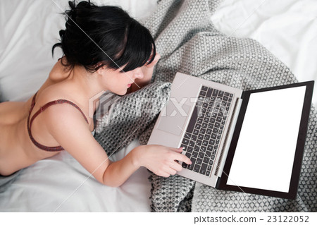 Naked woman using laptop with empty screen in bed 23122052