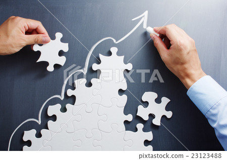 Construct growth strategy. Hand that assembles the puzzle in a staircase pattern and a hand drawing an arrow rising on the blackboard. 23123488