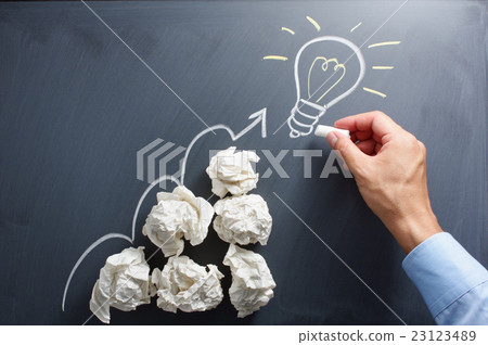 A hand drawing a stacked paper waste and a light bulb lit on a blackboard 23123489