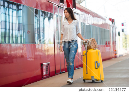 Young happy woman with luggage at a train station  23154377