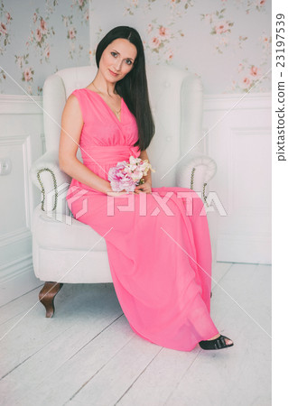 Brunette girl in pink dress sitting white armchair 23197539
