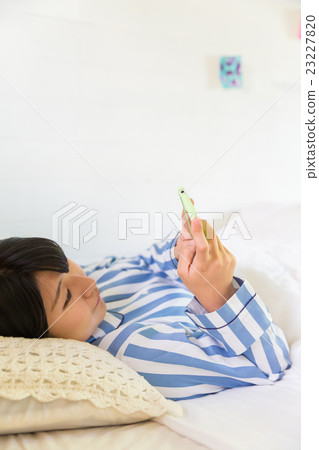 一名婦女在床上的看一個智能手機 一名婦女在床上的看一個智能手機 23227820