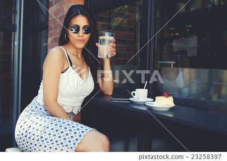 Latin woman in sunglasses enjoying beverage  23258397