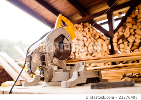 Circular saw laid on table, stack of wood behind 23276493