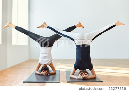 Two young women doing yoga asana open angle pose in headstand 23277856