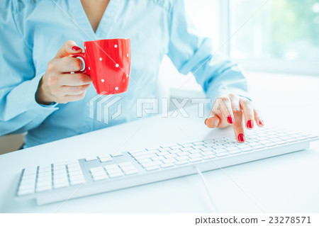 Woman office worker typing on the keyboard and drinking coffee 23278571