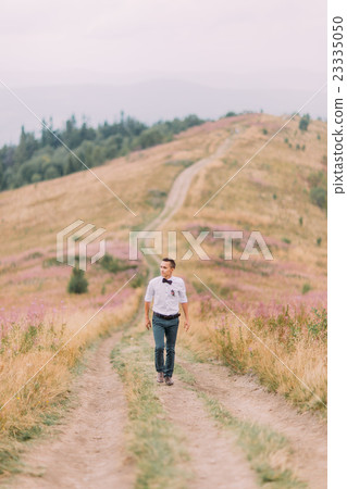 Stylish groom walks on the meadow. Alpian Stylish groom walks on the meadow. Alpian 23335050