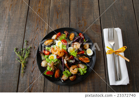 Portion of seafood salad with cutlery on wood 23372740