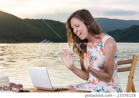 Woman having a video call by the lake 23376159
