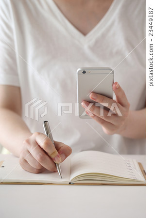 採取筆記的婦女，當觀看智能手機時 23449187