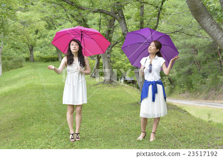 Two women walking while holding an umbrella Two women walking while holding an umbrella 23517192