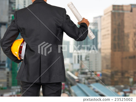 engineer in suit holding orange helmet and blueprint on abstract Blurred photo of sky train with cityscape background, business busy concept 23525002
