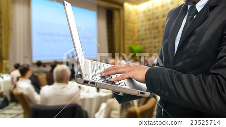 Businessman using the laptop on the Abstract blurred photo of conference hall or seminar room with attendee background Businessman using the laptop on the Abstract blurred photo of conference hall or seminar room with attendee background 23525714