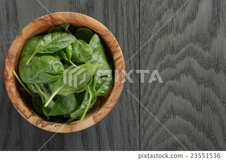 fresh spinach leaves in olive bowl on wood table 23551536