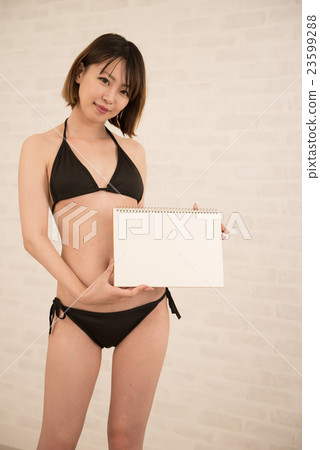 A female model wearing a black bikini with a white board in hand A female model wearing a black bikini with a white board in hand 23599288