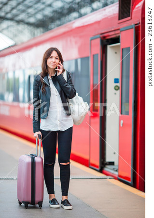 Young woman with luggage talking by cellphone at a Young woman with luggage talking by cellphone at a 23613247
