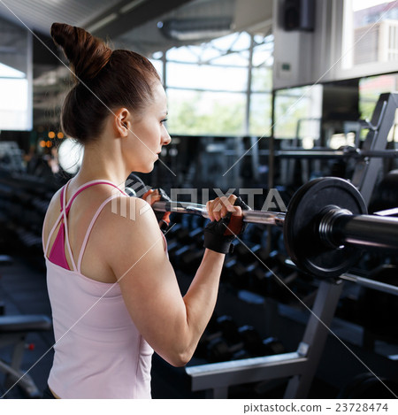 Young beautiful woman training biceps with barbell 23728474