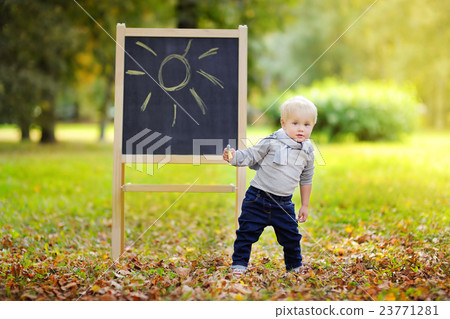 Toddler boy drawing standing by a blackboard 23771281