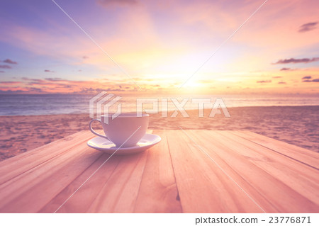 Coffee cup on wood table at sunset or sunrise beach with lens flare. Warm toning effect. Retro and vintage style Coffee cup on wood table at sunset or sunrise beach with lens flare. Warm toning effect. Retro and vintage style 23776871