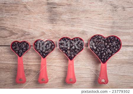 Coffee beans in red heart plastic cup on wooden table top view Coffee beans in red heart plastic cup on wooden table top view 23779302