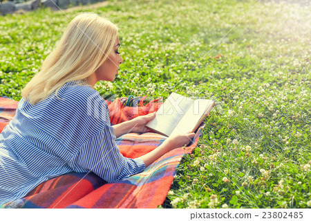 Profile of blonde girl read book on green grass 23802485