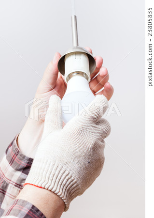 Electrician mounts new LED lamp in lampholder 23805835