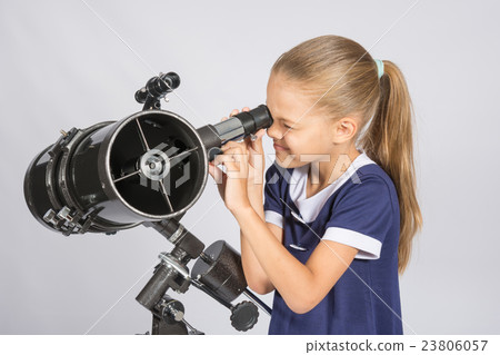 Seven-year girl squinting with interest looks in a reflector telescope 23806057