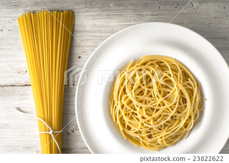 Raw and cooked spaghetti on the white wooden table 23822622