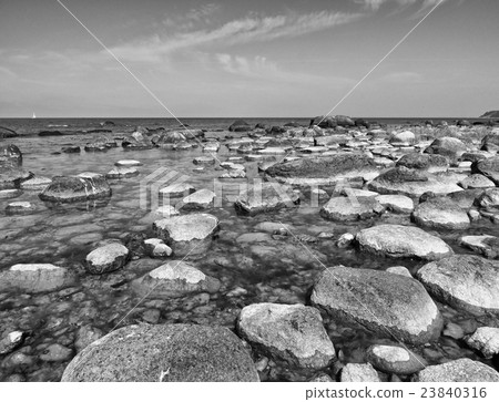 Big boulders in shore in  smooth wavy sea. 23840316