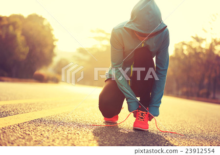young fitness woman runner tying shoelace on road 23912554