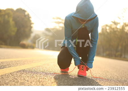 young fitness woman runner tying shoelace on road 23912555
