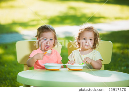 Two little girls sitting at a table and eating Two little girls sitting at a table and eating 23917878