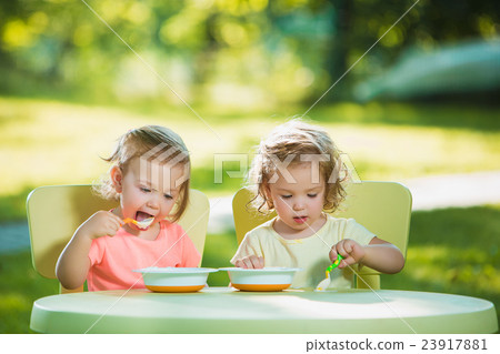 Two little girls sitting at a table and eating 23917881