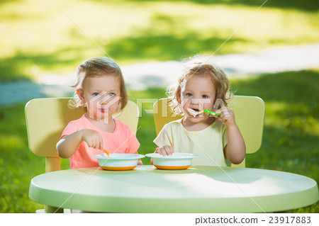 Two little girls sitting at a table and eating Two little girls sitting at a table and eating 23917883